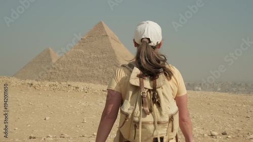 Woman tourist walking on sandy plateau towards pyramids of Giza on a clear sunny day, a visitor exploring the sights of ancient Egypt in Cairo