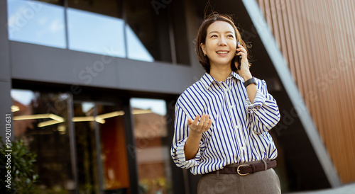 Korean woman talks on the phone outside a modern building in the afternoon sunlight