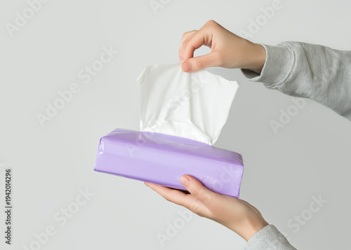 Hands pulling a white tissue from a purple packet