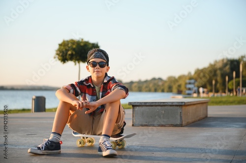Tableau sur toile A young skater boy sits calmly on a skateboard in a bustling skate park on a sun