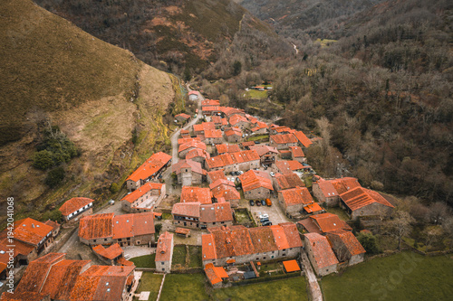 Stunning aerial drone perspective of Barcena Mayor, a historic mountain village in Cantabria. The image showcases the traditional stone houses.
