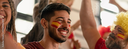 Excited football fans supproting spanish national team in live soccer match at stadium.