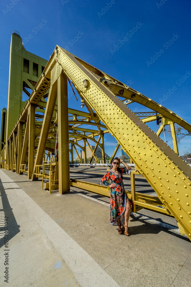 Fototapeta premium A woman stands in front of a yellow bridge, posing for a picture