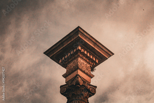 Fotografi Low angle shot of a decorative stone column capital under a dramatic sky