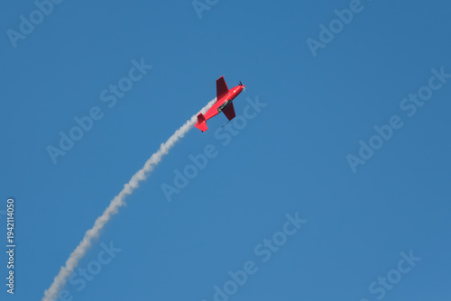 Quadro su tela Red stunt aerobatic plane in inverted flight performing stunts in blue sky