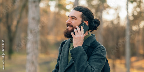 Bearded Man talking on smartphone in Autumn Park Wearing Wool Coat And Bun.