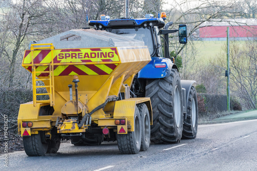 Tableau sur toile Tractor towing salt spreader on rural road for winter gritting