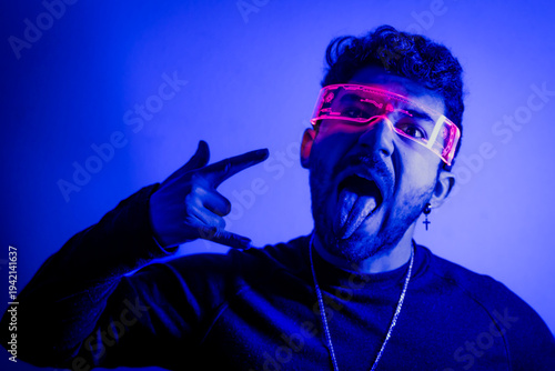 Bilde på lerret Young man wearing futuristic glasses making rock on gesture with tongue out