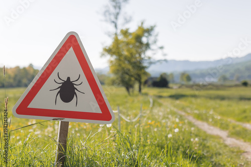 A sign warns of tick risks on a path in nature. Hikers should be aware of Lyme disease and tick-borne diseases while outdoors.