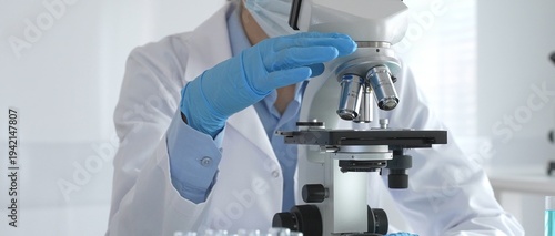 Scientist wearing protective gear carefully adjusting microscope lens, analyzing medical research samples with precision in sterile laboratory environment