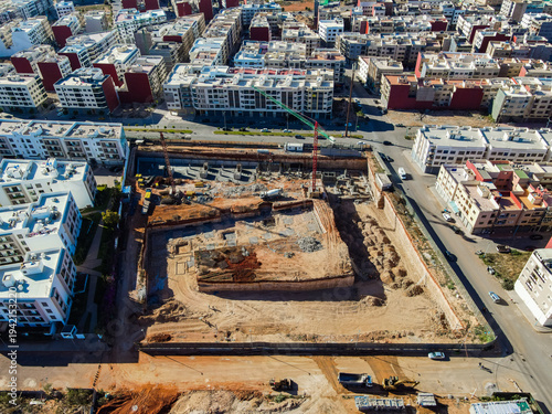 Aerial drone view of a large residential real estate development and construction site with cranes, foundations, and heavy machinery in Agadir, Morocco.