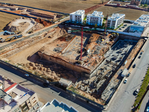 Aerial drone view of a large residential real estate development and construction site with cranes, foundations, and heavy machinery in Agadir, Morocco.