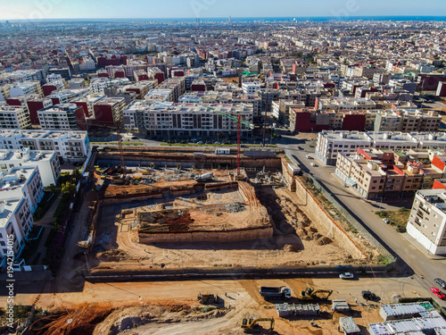Aerial drone view of a large residential real estate development and construction site with cranes, foundations, and heavy machinery in Agadir, Morocco.