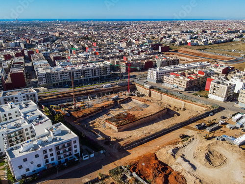 Aerial drone view of a large residential real estate development and construction site with cranes, foundations, and heavy machinery in Agadir, Morocco.