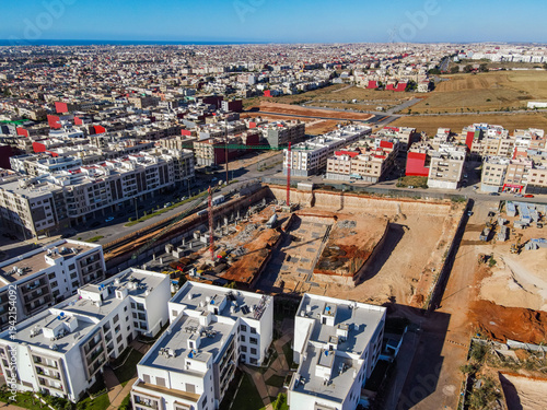 Aerial drone view of a large residential real estate development and construction site with cranes, foundations, and heavy machinery in Agadir, Morocco.