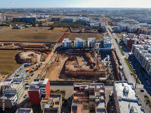 Aerial drone view of a large residential real estate development and construction site with cranes, foundations, and heavy machinery in Agadir, Morocco.
