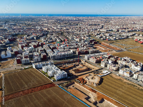 Aerial drone view of a large residential real estate development and construction site with cranes, foundations, and heavy machinery in Agadir, Morocco.