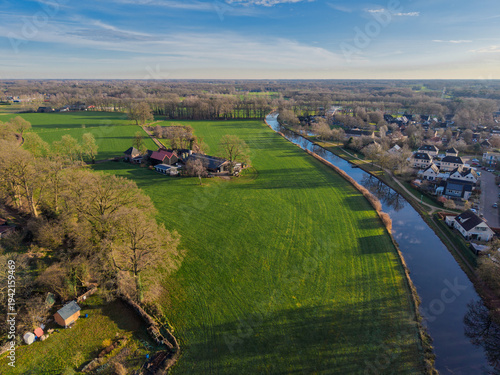 Foto Aerial view of a traditional farmhouse and lush green fields along a canal in the Dutch countryside during a golden hour sunset