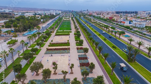 Aerial drone view of a newly renovated modern avenue featuring green public parks, sports courts, palm trees, and urban infrastructure in Agadir, Morocco.