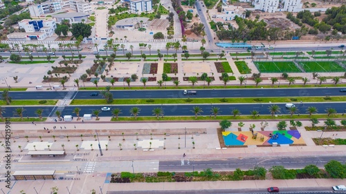 Aerial drone view of a newly renovated modern avenue featuring green public parks, sports courts, palm trees, and urban infrastructure in Agadir, Morocco.