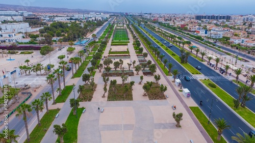 Aerial drone view of a newly renovated modern avenue featuring green public parks, sports courts, palm trees, and urban infrastructure in Agadir, Morocco.