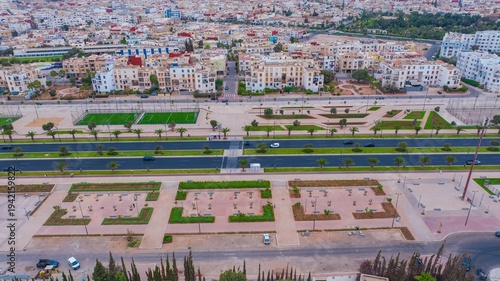 Aerial drone view of a newly renovated modern avenue featuring green public parks, sports courts, palm trees, and urban infrastructure in Agadir, Morocco.