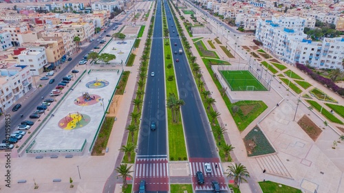 Aerial drone view of a newly renovated modern avenue featuring green public parks, sports courts, palm trees, and urban infrastructure in Agadir, Morocco.