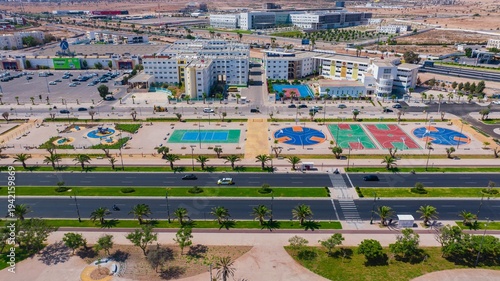 Aerial drone view of a newly renovated modern avenue featuring green public parks, sports courts, palm trees, and urban infrastructure in Agadir, Morocco.