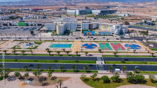 Aerial drone view of a newly renovated modern avenue featuring green public parks, sports courts, palm trees, and urban infrastructure in Agadir, Morocco.