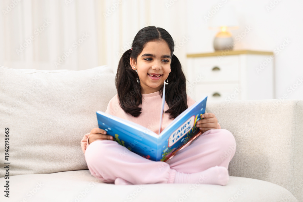 Obraz premium Cute little girl reading book on couch at home