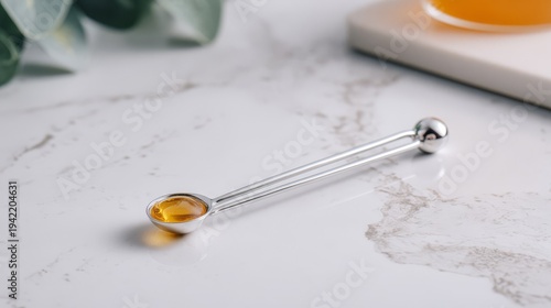 Silver measuring spoon with golden honey on marble surface