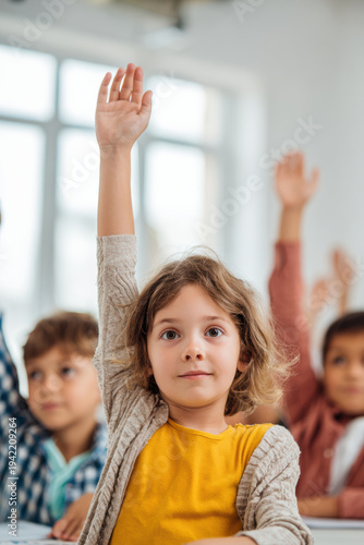 Wallpaper Mural Education training class. Knowledge learning improvement study. A young girl raising her hand in a classroom, surrounded by other children. On the table in front of her are papers. Torontodigital.ca