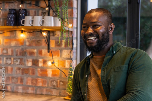 African American man smiling while sitting at counter in cafe wearing green shirt, ceramic mugs