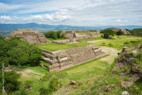 Ancient Monte Alban ruins under bright sky with lush green fields and distant mountains in Oaxaca Mexico