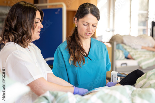 Clinical instructor guiding nursing student during wound dressing change on patient in hospital ward