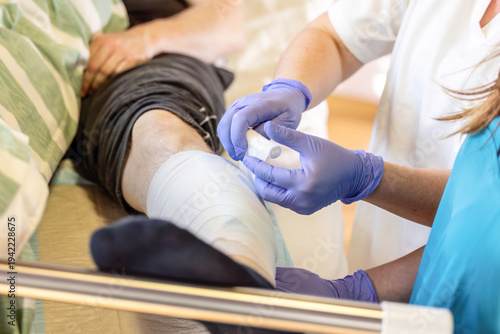Nurse performing wound dressing change on patient leg during clinical nursing care in hospital ward