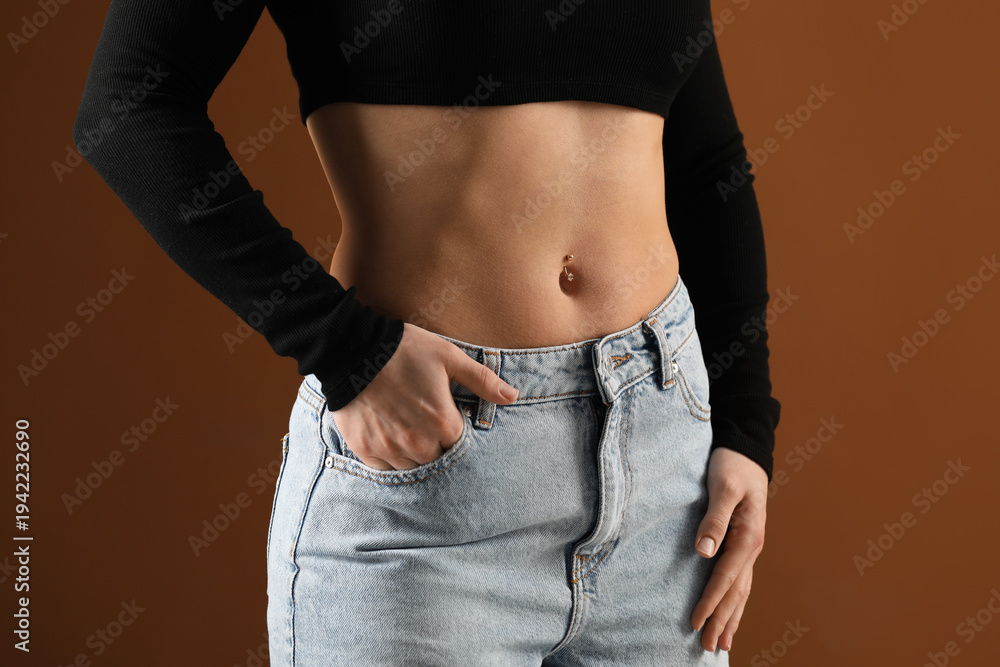 Fototapeta premium Woman with belly button piercing on brown background, closeup
