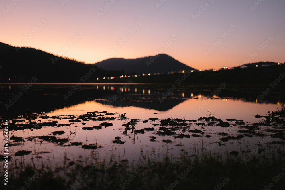 Naklejka premium Lake reflecting twilight sky and distant city lights