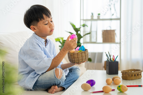 Cute asian little boy holding and looking at pink Easter egg at table in living room, Happy child playing with spring holiday decoration, Childhood development and fun celebration concept, Easter day