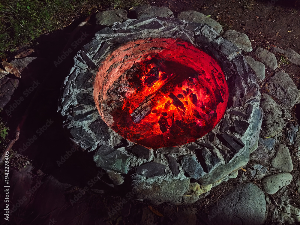 Naklejka premium Night photo of bonfire in stone fire pit. Flame of burning wood in camp at night.