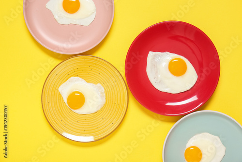 Plates with tasty fried eggs on yellow background