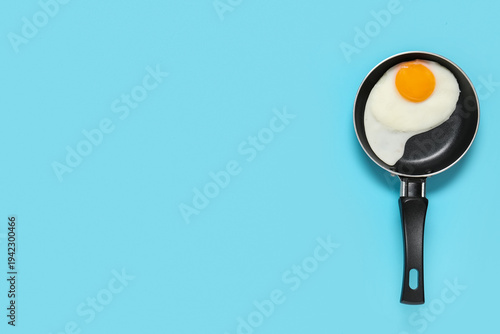 Frying pan with tasty fried egg on blue background