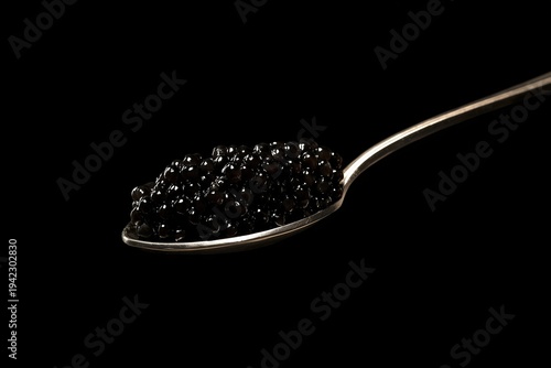 Black caviar in spoon on ice close up on black background 