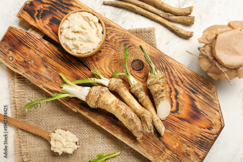 Bowl and jar of horseradish sauce with roots on light grunge background