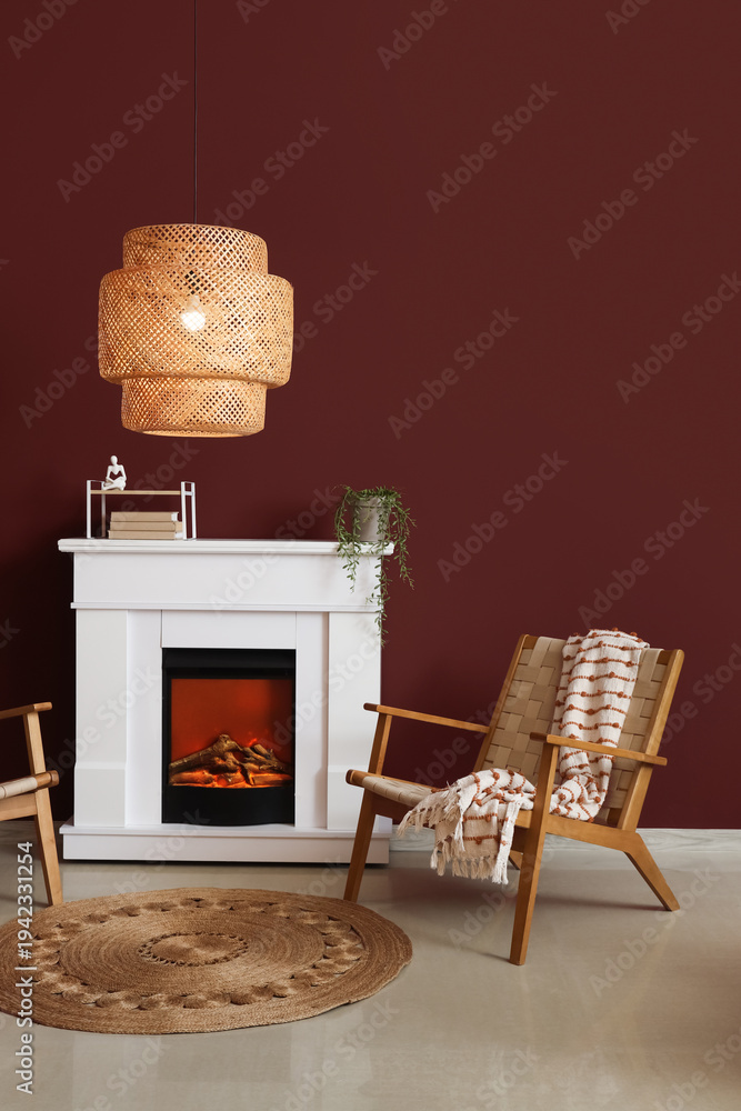 Fototapeta premium Interior of stylish living room with cozy armchair, fireplace and glowing lamp near red wall