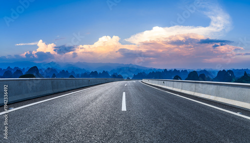 Empty asphalt road winding through karst mountain peaks under a sunset sky in Guilin, China. Road trip and travel concept.