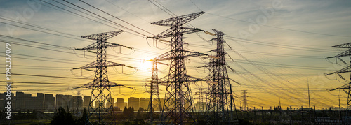 Quadro su tela High-voltage power lines and electricity pylons against a sunset sky with urban city skyline