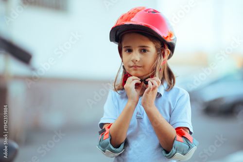 Portrait of Girl Wearing Elbow Pads Putting a Red Helmet On. Cute adorable kid feeling ready to go for a ride 
