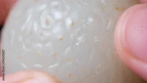 Close-up of finger holding a white strawberry with tan seeds on a shiny surface