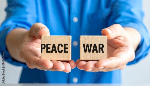 Two hands holding wooden blocks labeled PEACE and WAR against a blue sky with clouds, with PEACE above WAR, symbolizing peace prevailing over conflict, harmony, and the triumph of nonviolence.
